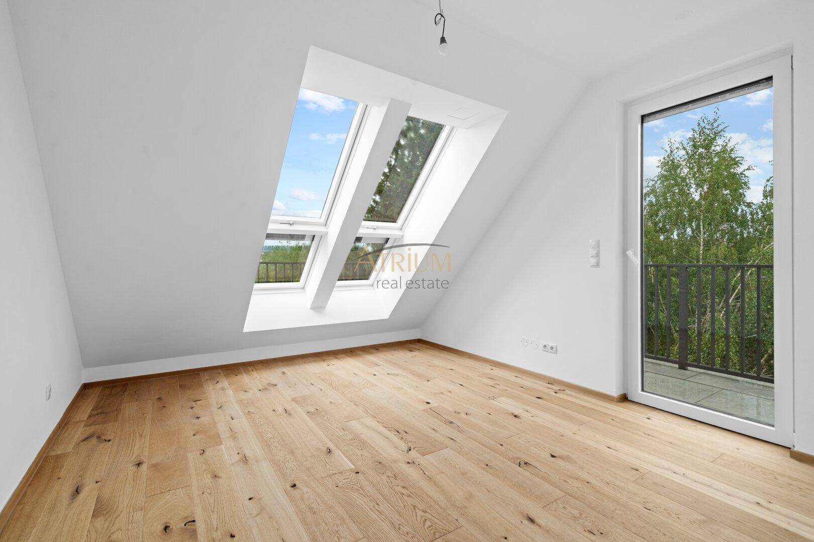 Helles Zimmer mit Holzboden, Dachfenstern und Zugang zu einem französischen Balkon.