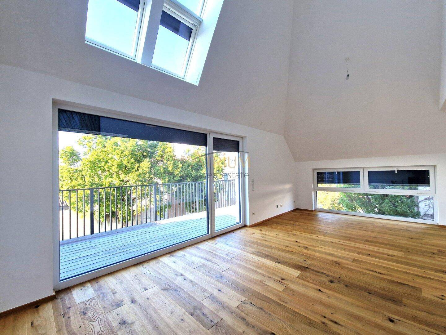 Geräumiges, leeres Wohnzimmer mit Holzboden, hohen Decken, Dachfenstern und Zugang zu einem Balkon.