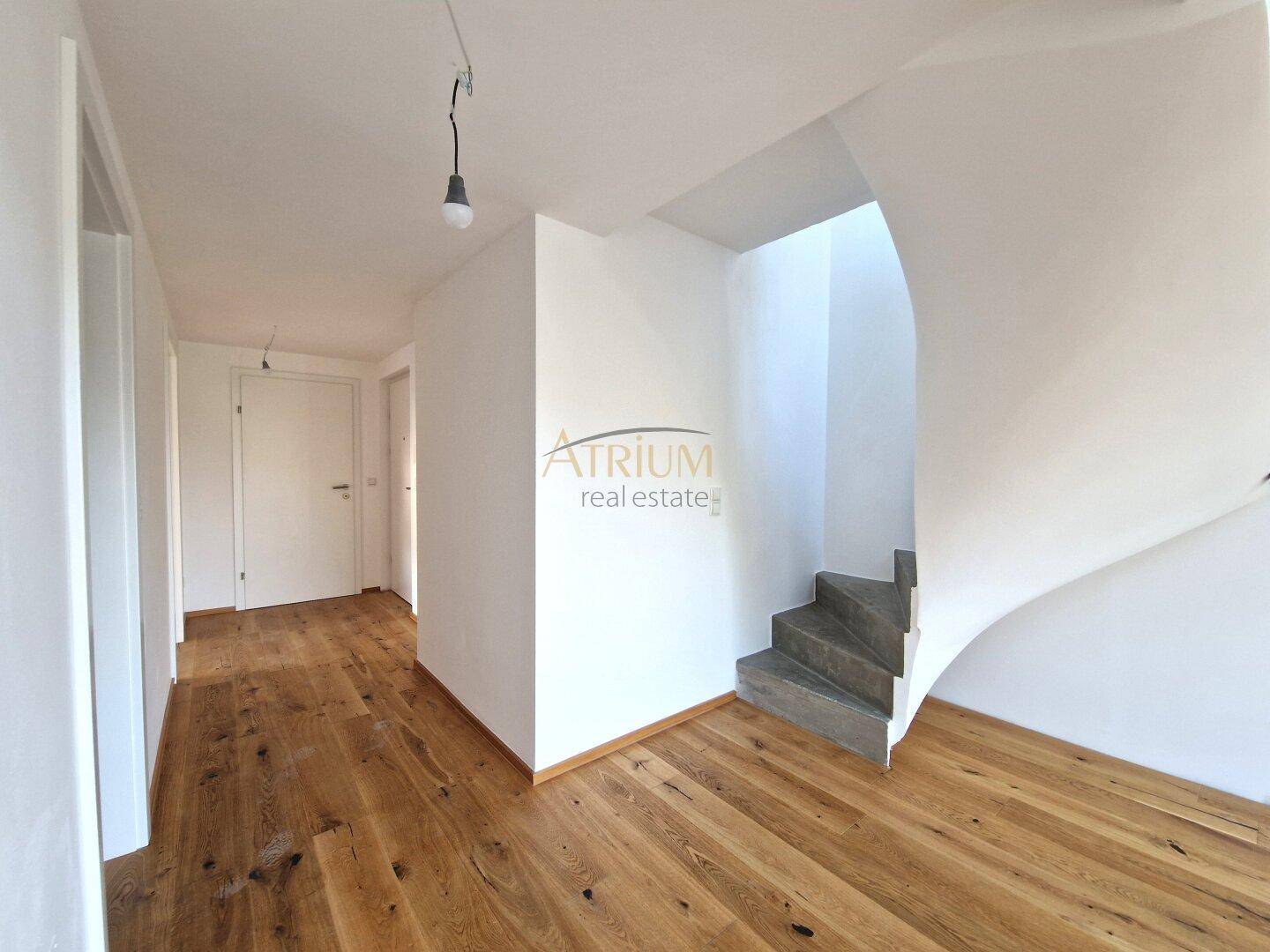 Heller Flurbereich mit Holzboden und einer elegant geschwungenen Treppe, die in die obere Etage führt.