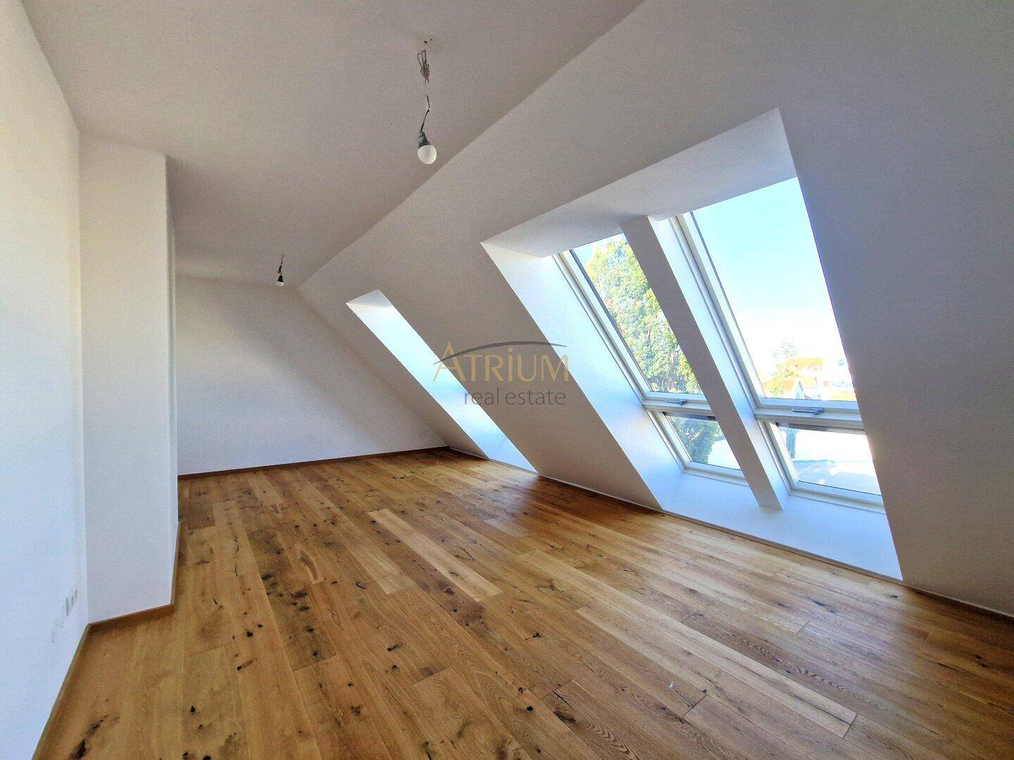 Leeres Schlafzimmer mit Holzboden, schrägen Decken und großen Dachfenstern, bietet viel natürliches Licht.