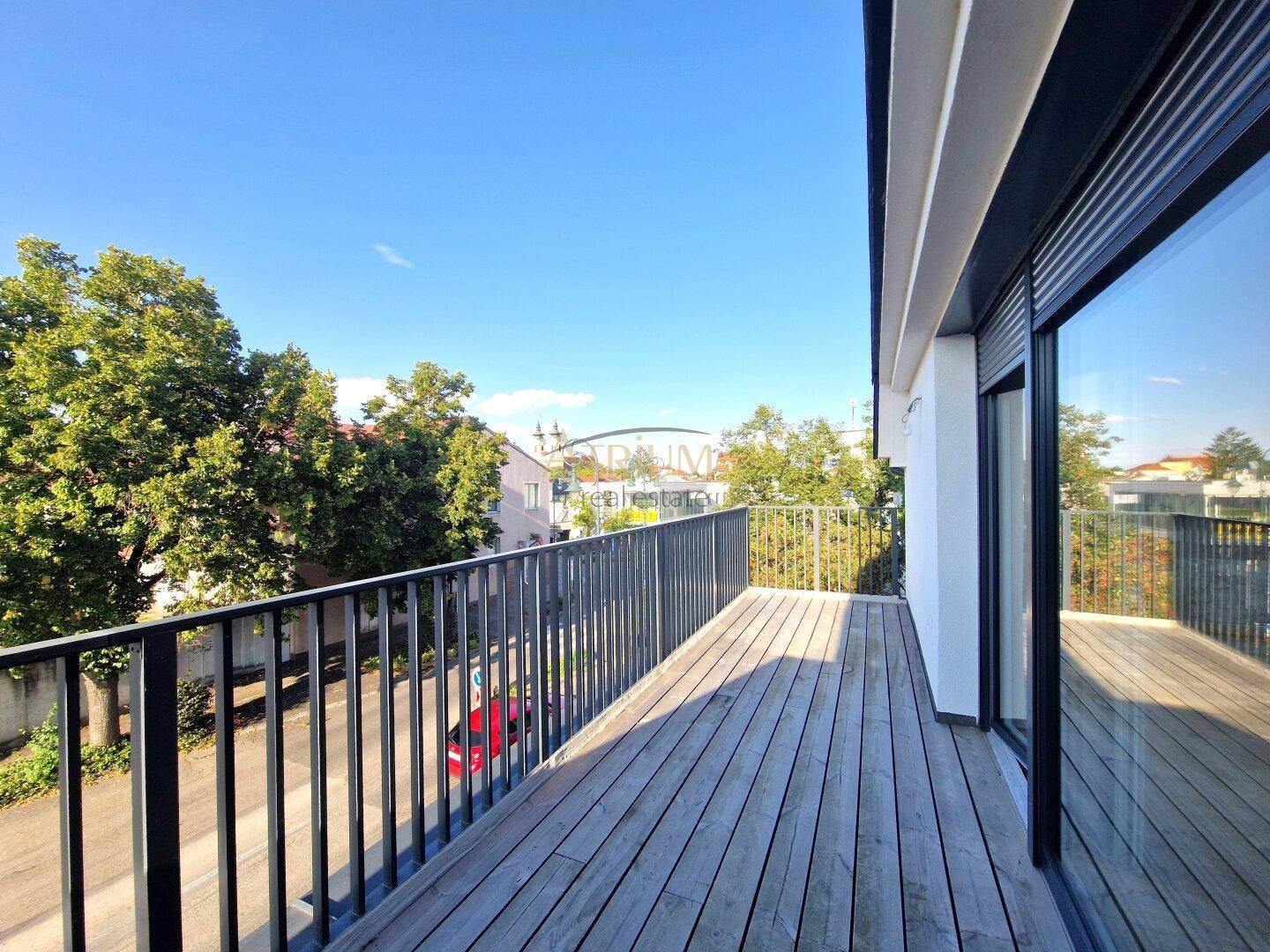 Geräumiger Balkon mit Holzboden und Metallgeländer, bietet einen Blick auf die umliegende Grünfläche.