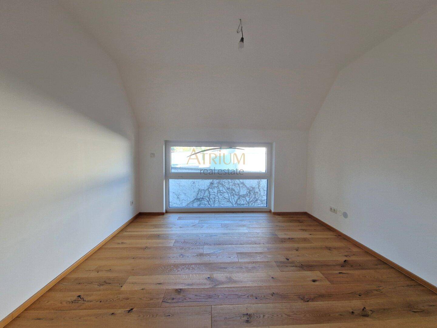 Heller Raum mit Holzboden, schrägen Decken und einem breiten Fenster, ideal als Schlaf- oder Arbeitszimmer.