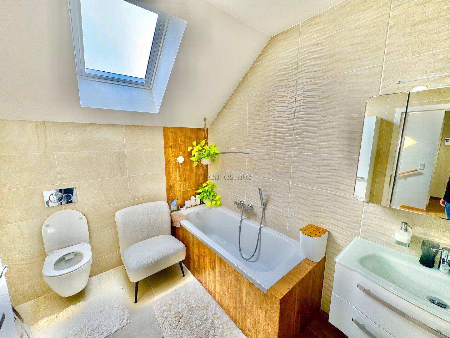 Modernes Badezimmer im Dachgeschoss mit Badewanne, WC und Dachfenster.