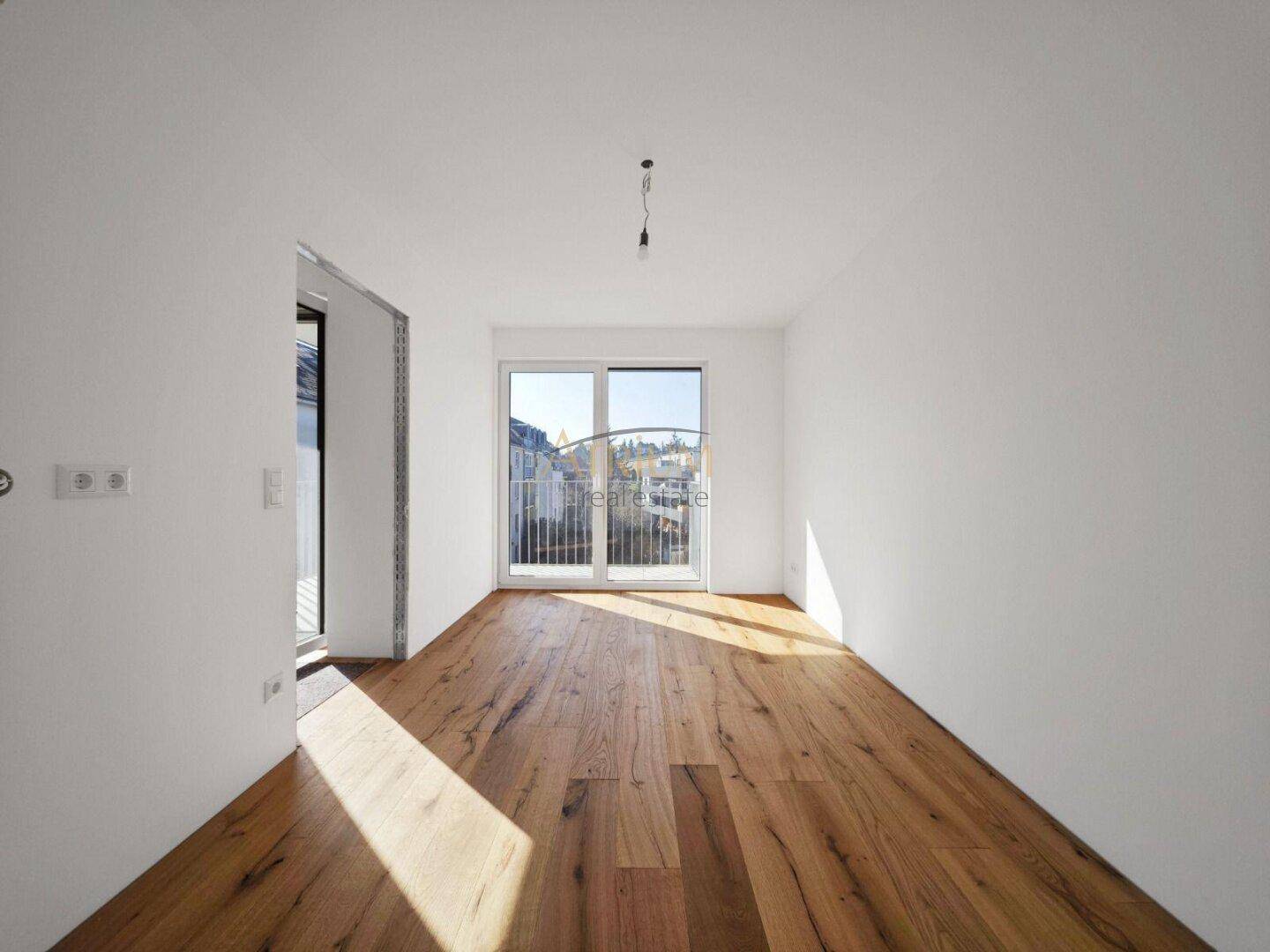 Heller Raum mit breiten Holzdielen, weißen Wänden und französischem Balkon.