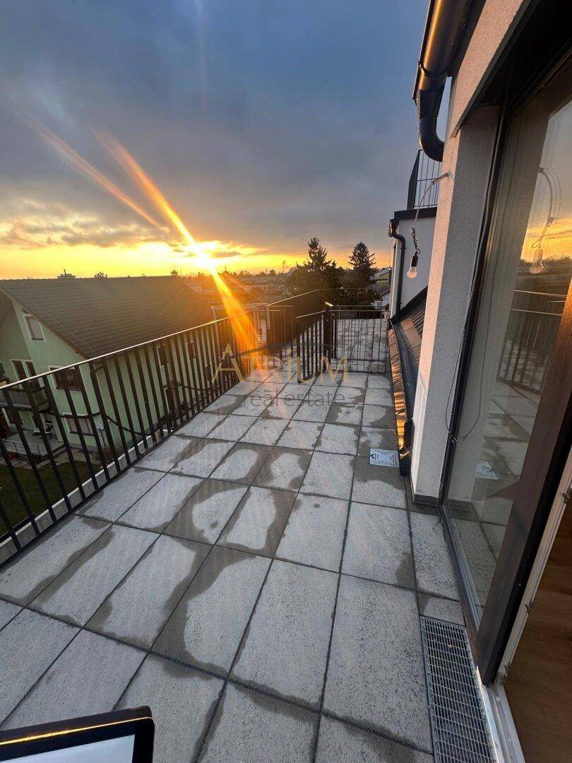 Geräumiger Balkon mit Fliesenboden und weitem Blick über die Dächer bei Sonnenuntergang.