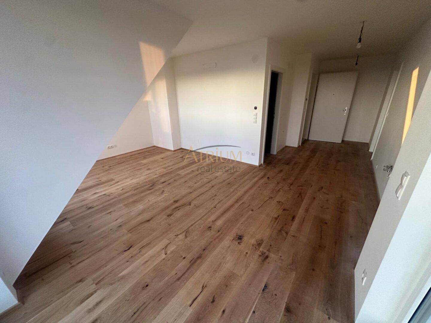 Geräumiger, leerer Raum mit Holzdielenboden und Dachschräge, bereit zum Einzug.