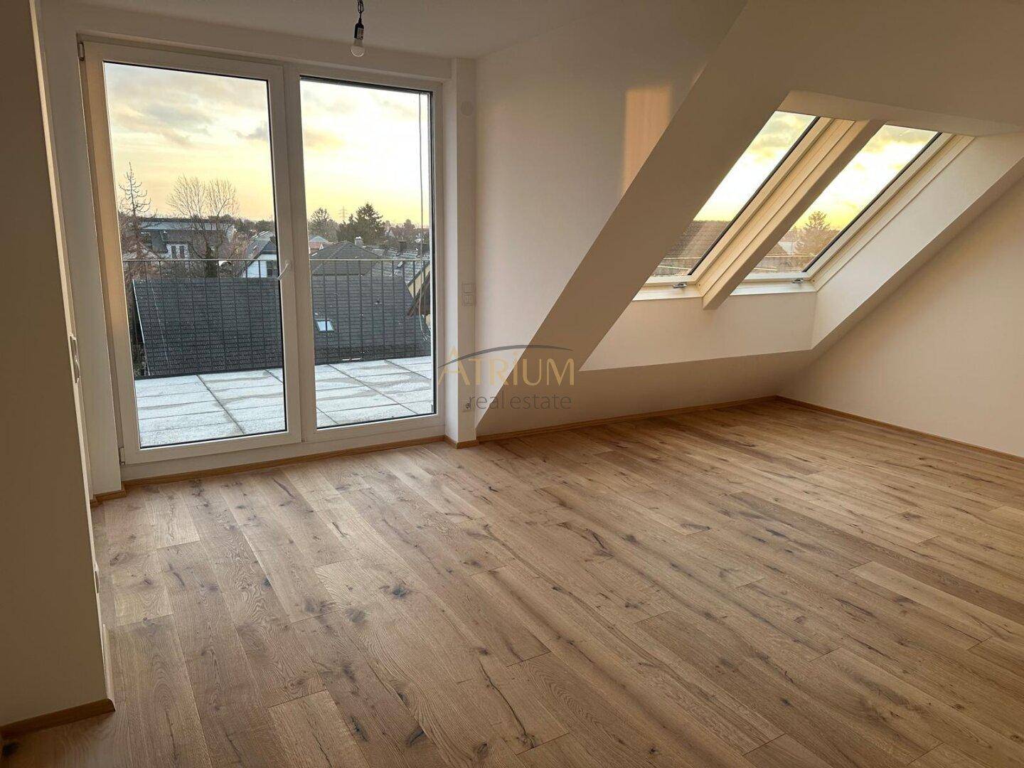 Heller Raum mit Holzdielen, Dachschrägen, Dachfenstern und Zugang zu einer Terrasse.