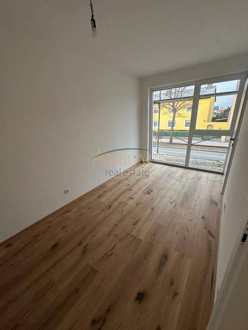 Heller Raum mit Holzdielenboden und großem Fenster mit Blick auf die Straße.