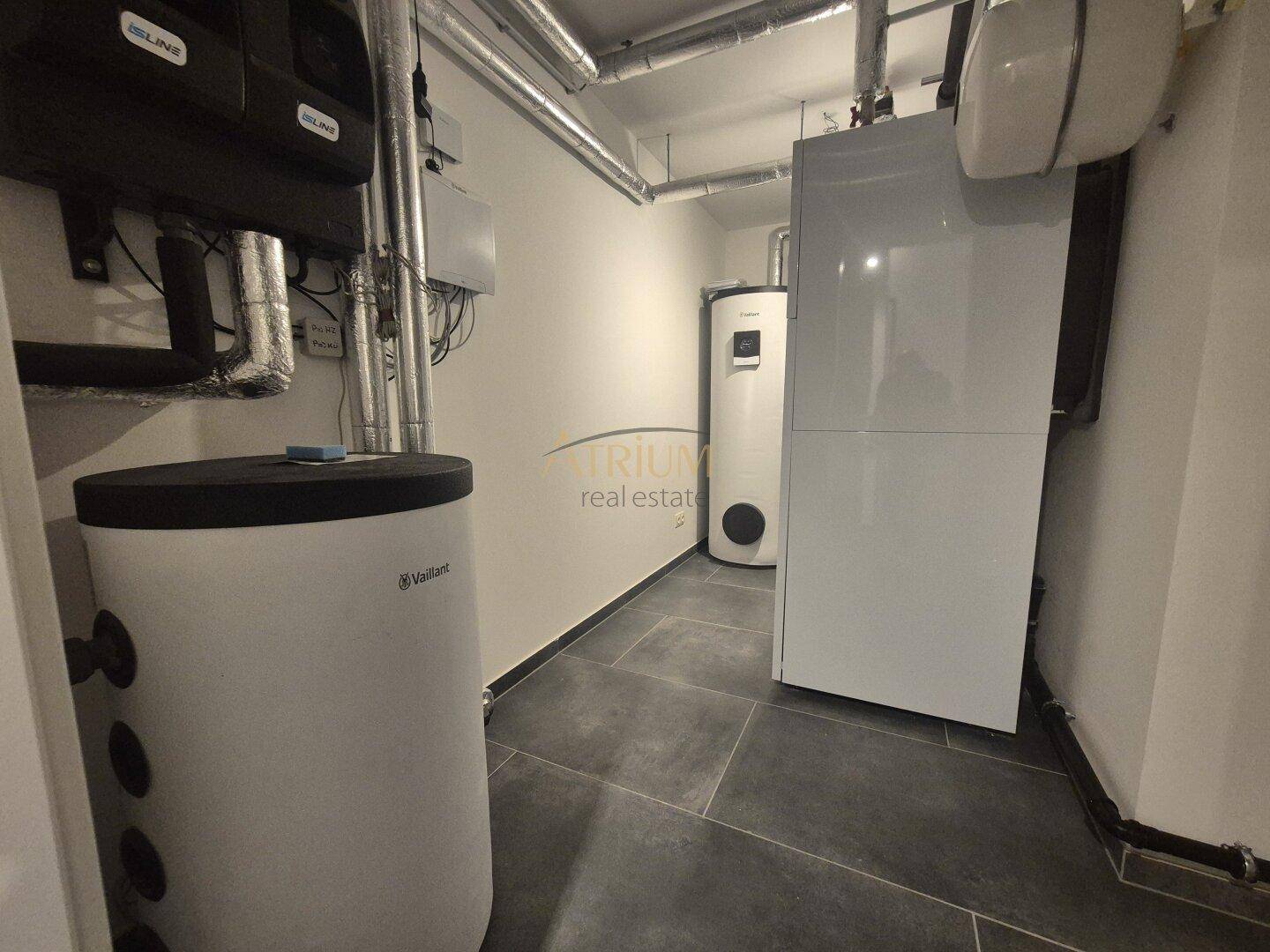 Technikraum im Keller mit modernen Heizungsanlagen und Warmwasserspeichern auf Fliesenboden.