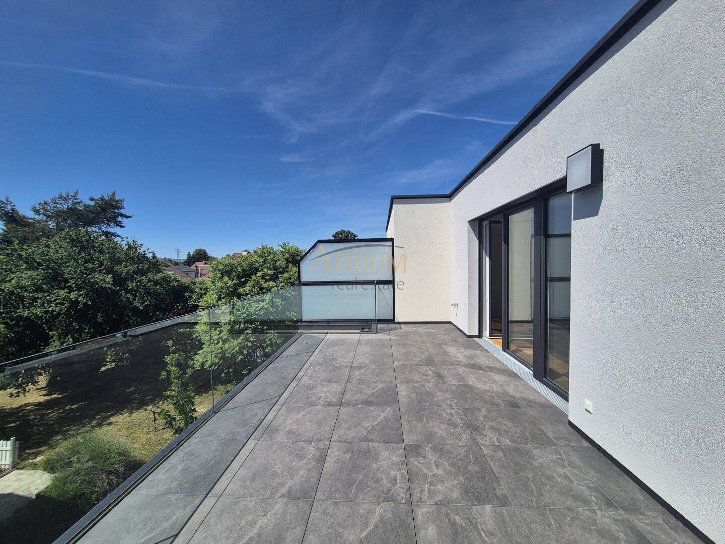 Weitläufige Terrasse mit elegantem Glasgeländer und Blick ins Grüne, perfekt für sonnige Tage.