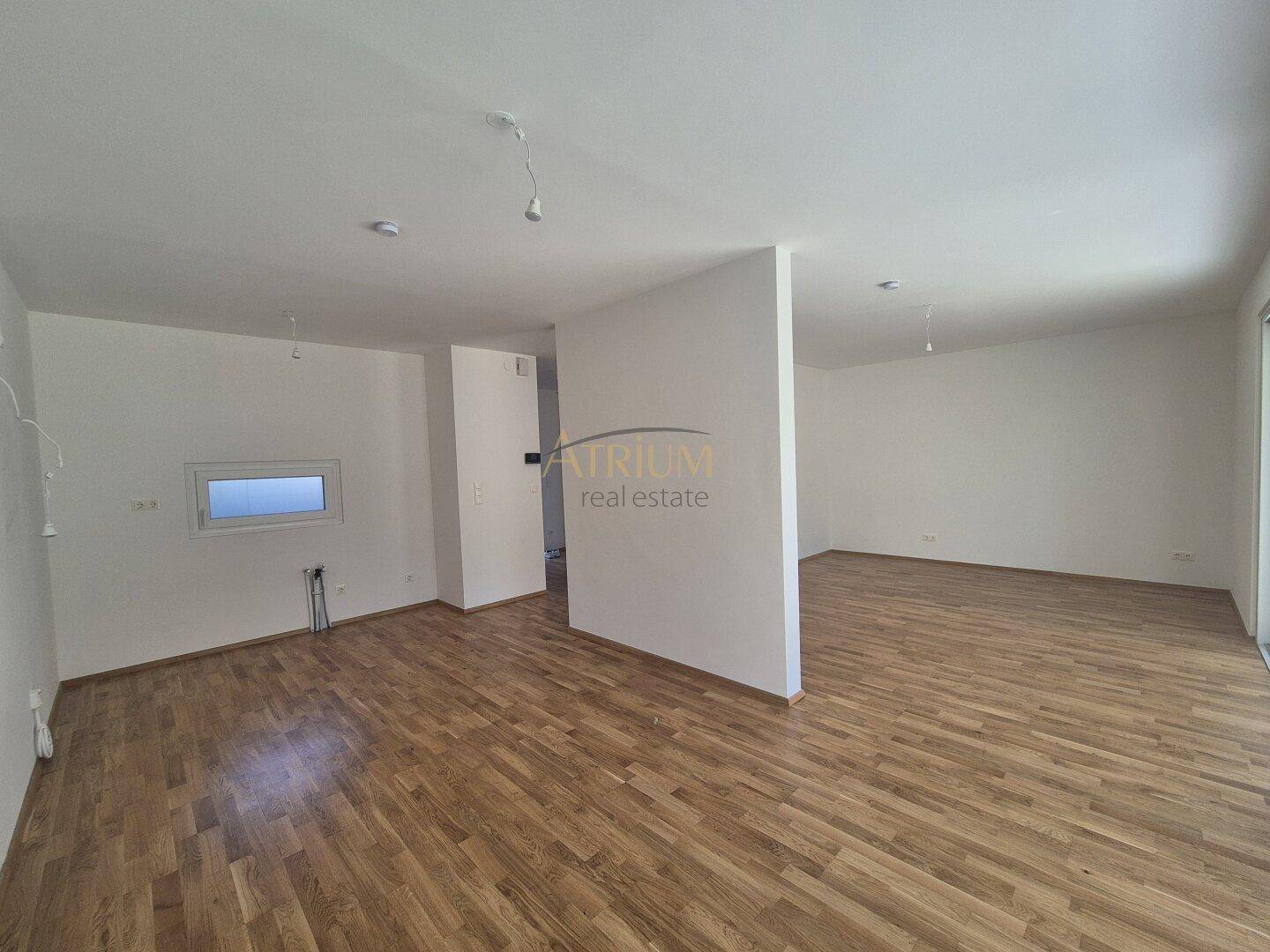 Geräumiger, heller Wohnbereich mit Holzboden und viel Tageslicht durch große Fenster.