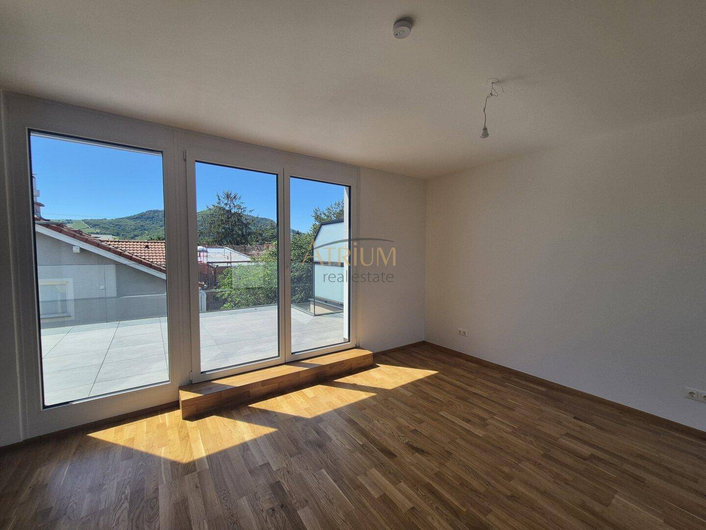 Lichtdurchflutetes Zimmer mit Holzboden und direktem Zugang zur Terrasse mit Bergblick.