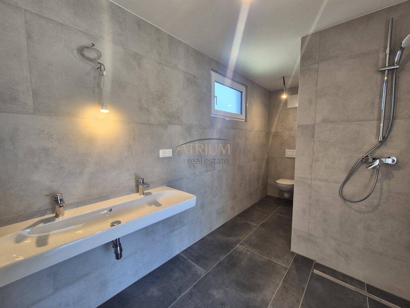 Modernes Badezimmer mit grauen Fliesen, Doppelwaschbecken und einer geräumigen begehbaren Dusche.