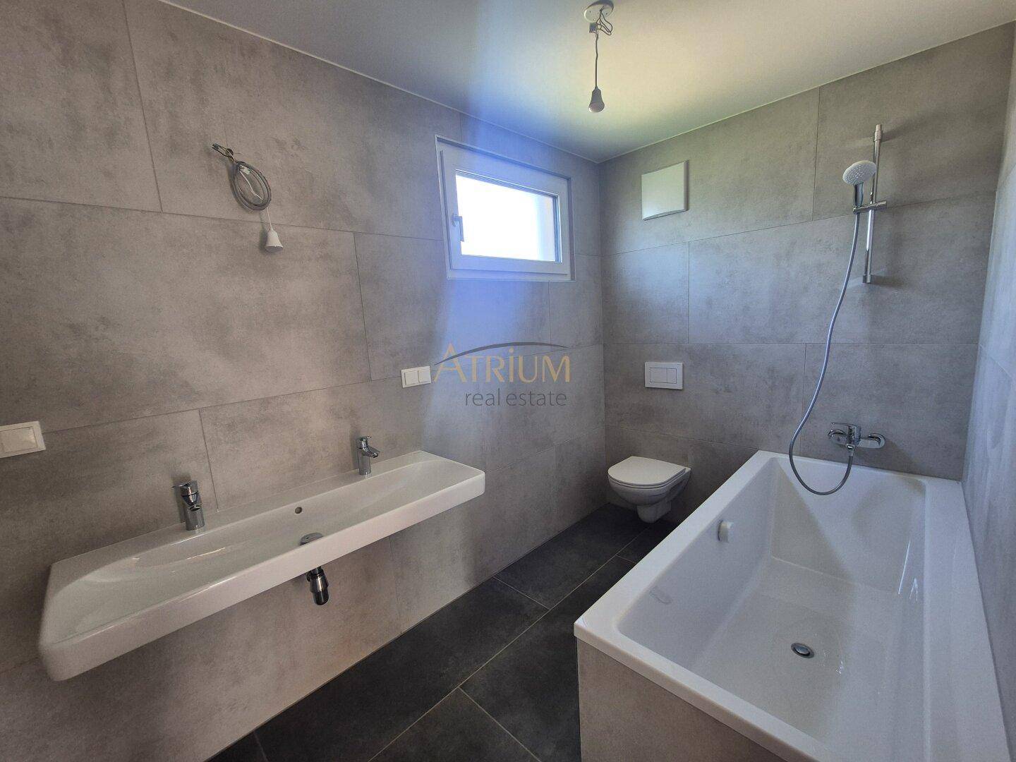 Zeitgemäßes Badezimmer mit grauen Fliesen, Doppelwaschbecken und einer modernen Badewanne.