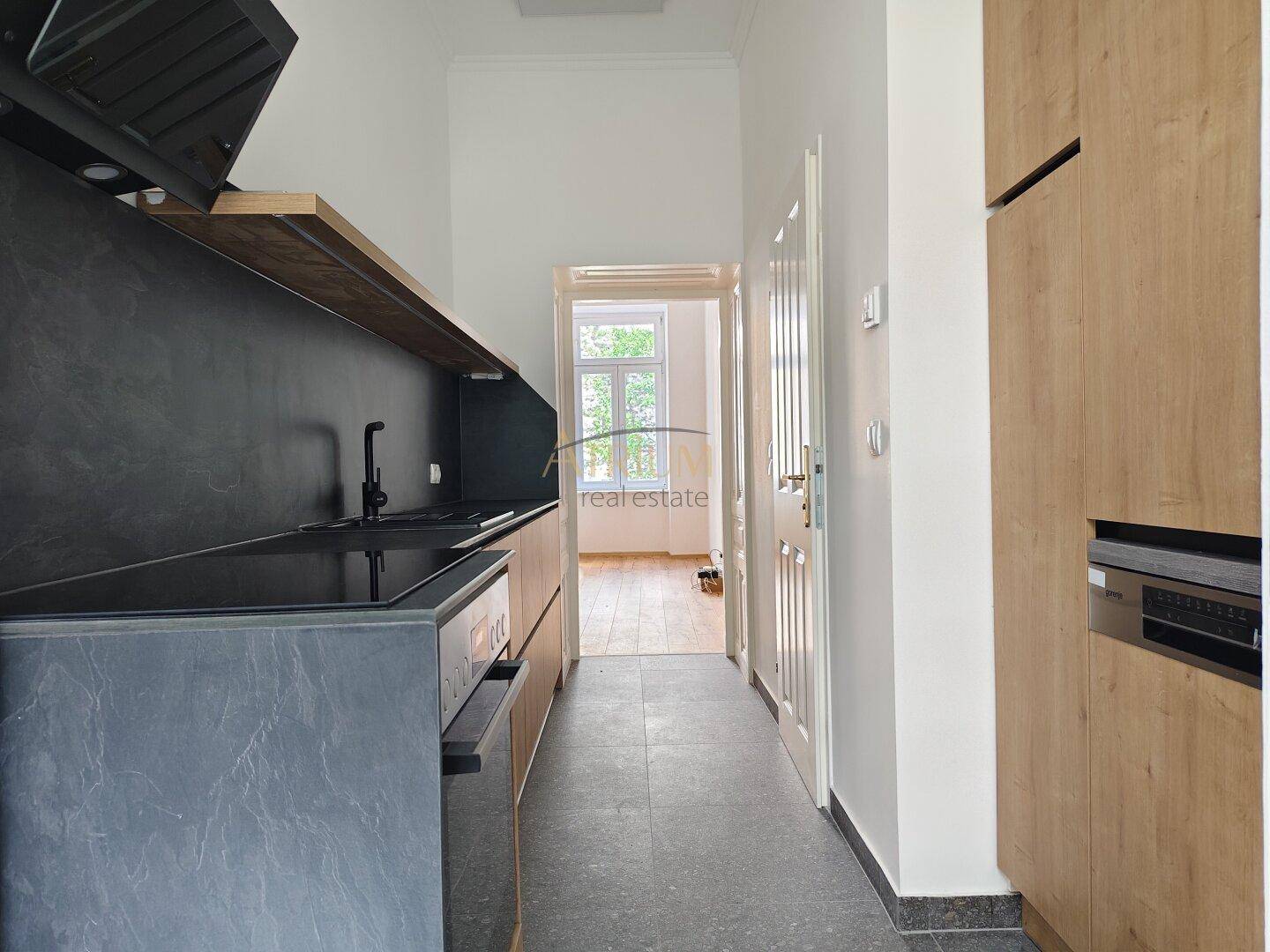 Moderne Küche mit dunklen Arbeitsplatten, Holzschränken und Blick in einen angrenzenden Raum.