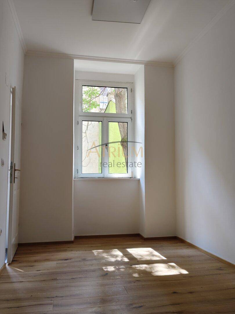 Heller Raum mit Holzboden und einem einzelnen Fenster, das Sonnenlicht auf den Boden wirft.