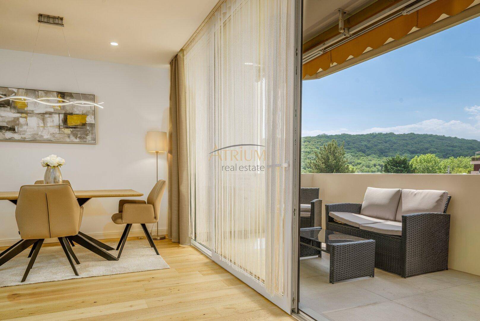 Essbereich mit Blick auf den möblierten Balkon und die umliegende grüne Landschaft.