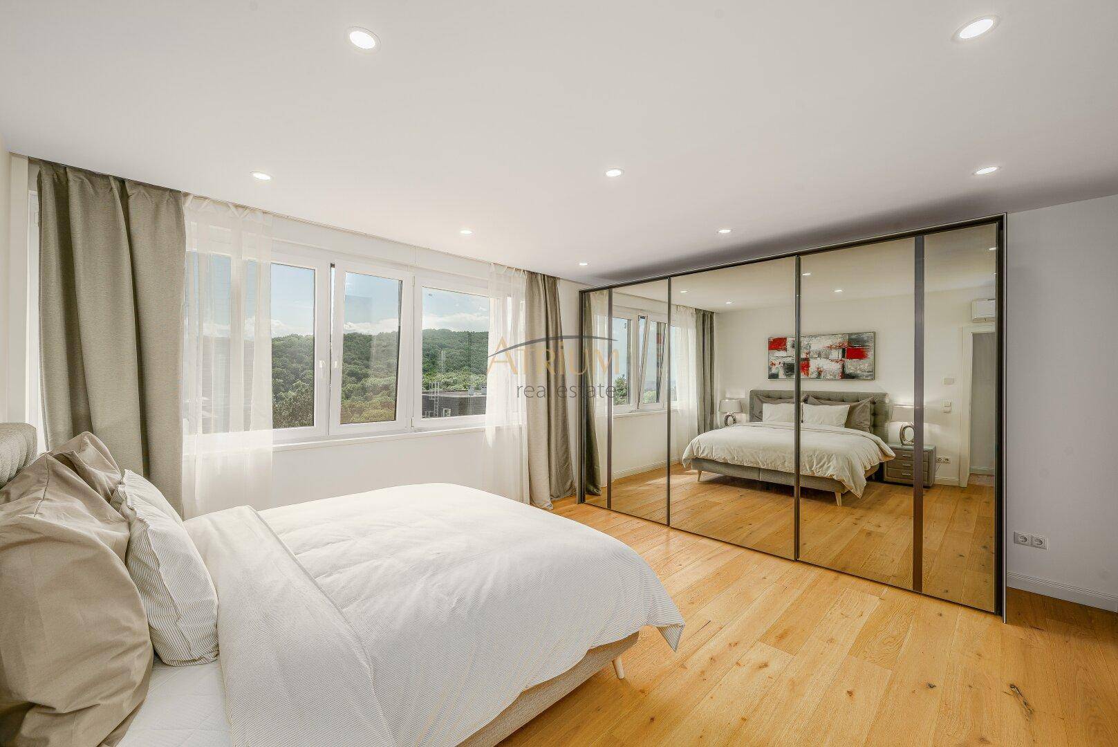 Helles Schlafzimmer mit großem Bett, Spiegelschränken und Fenster mit Blick ins Grüne.