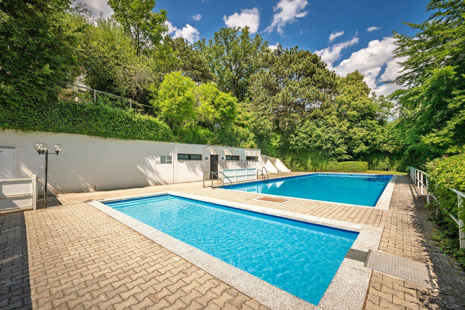 Attraktiver Außenpoolbereich mit zwei Schwimmbecken, umgeben von üppigem Grün.