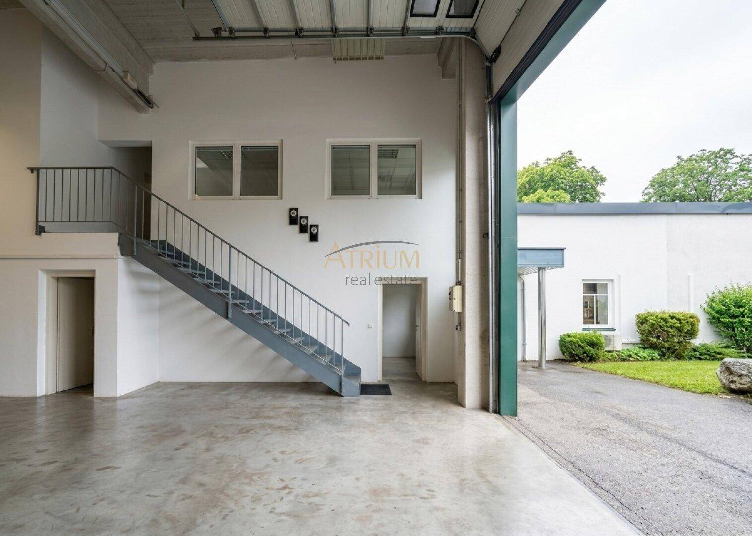 Heller Eingangsbereich einer Lagerhalle mit Rolltor, Treppe und Blick ins Grüne.