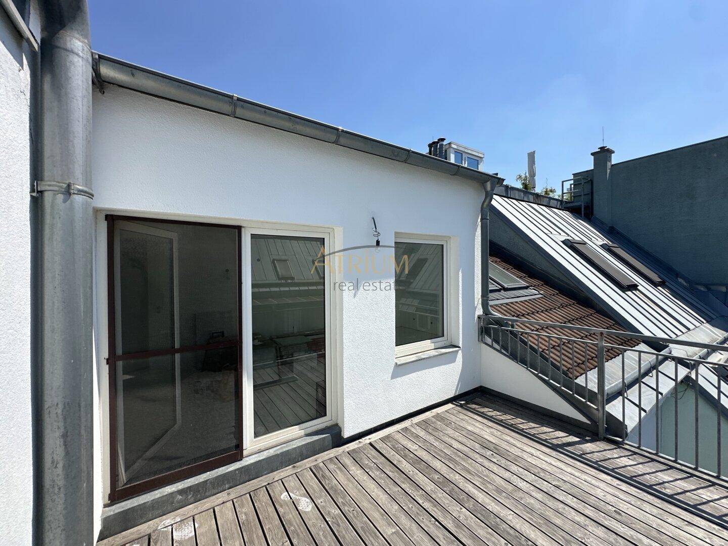 Dachterrasse mit Holzboden und Zugang zu einem Innenraum, umgeben von Dächern.