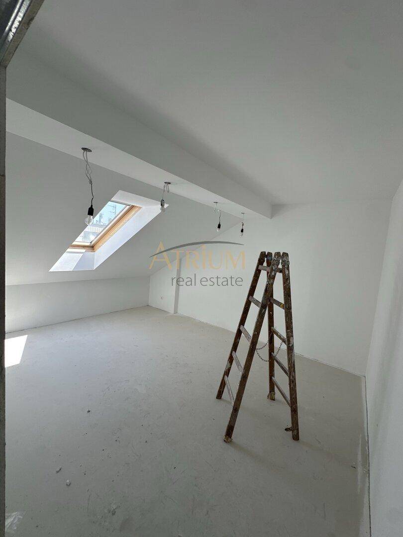 Unfertiger Raum mit Dachschräge und Dachfenster, eine Leiter steht im Vordergrund.