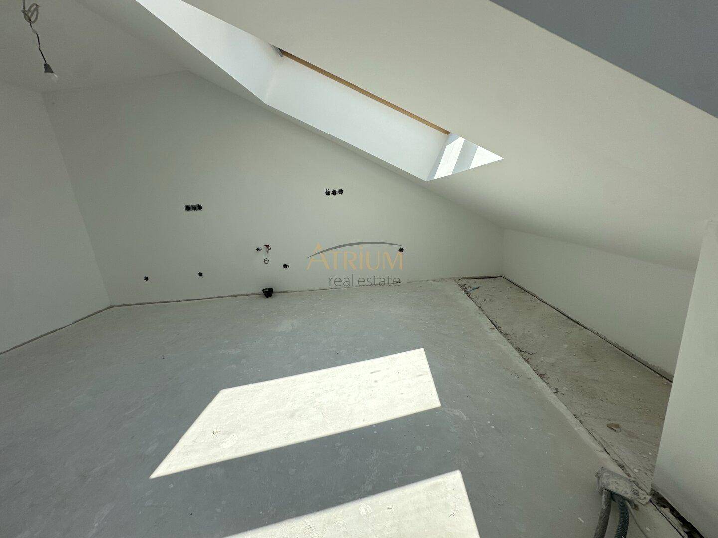 Unfertiger Raum mit Dachschräge und Dachfenster, bereit für den Innenausbau.