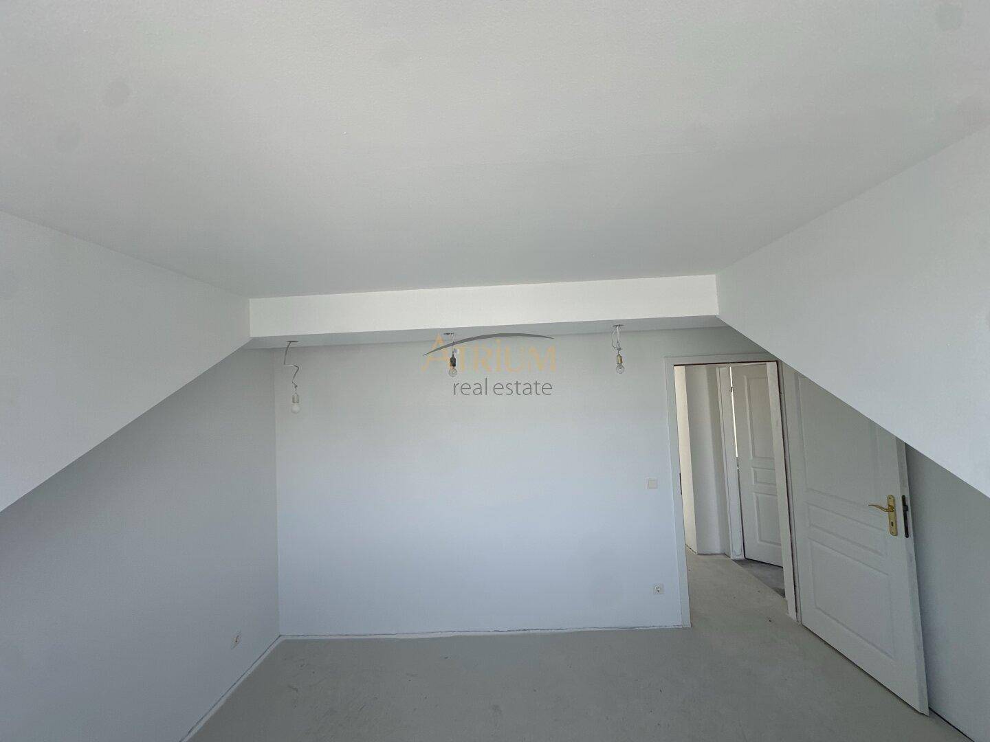 Unfertiger Raum mit Dachschräge und Tür, bereit für den Innenausbau.