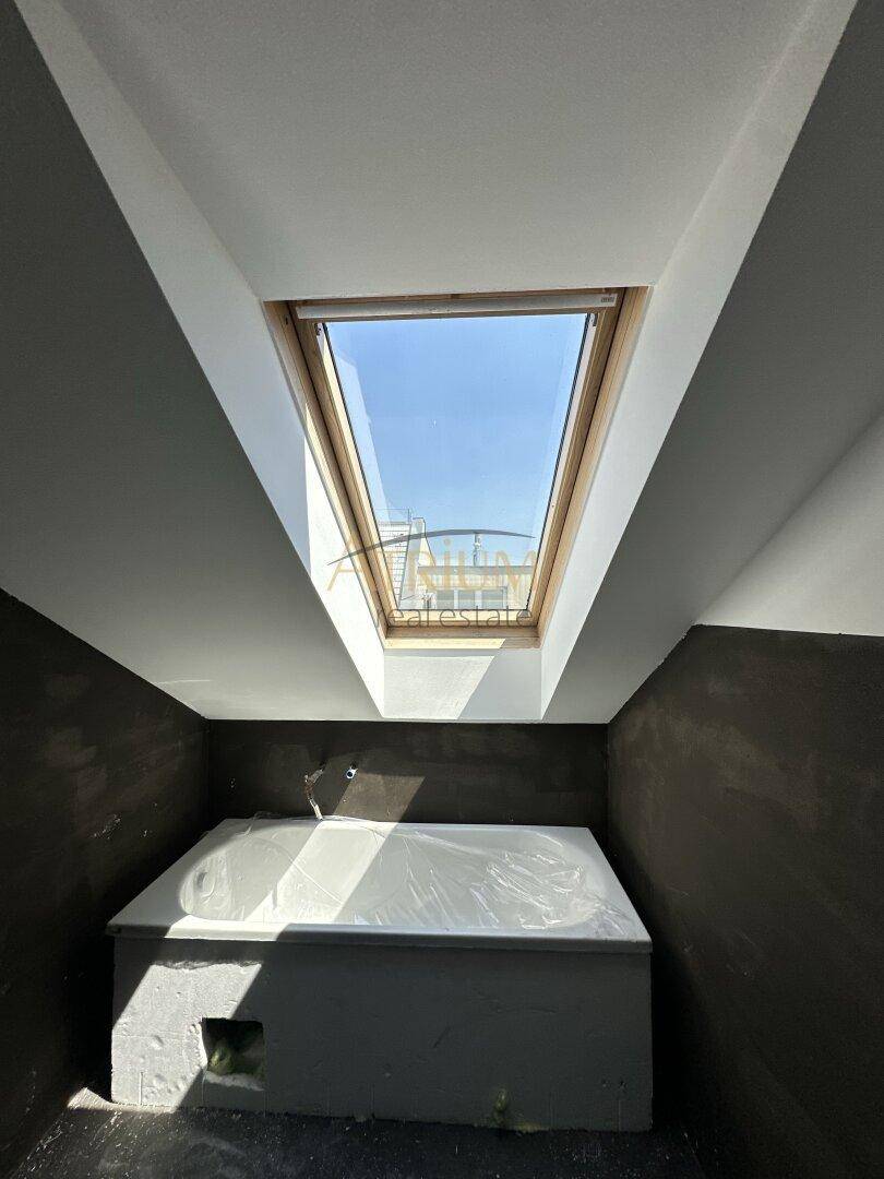 Unfertiges Badezimmer mit Badewanne unter einem großen Dachfenster, viel Tageslicht.