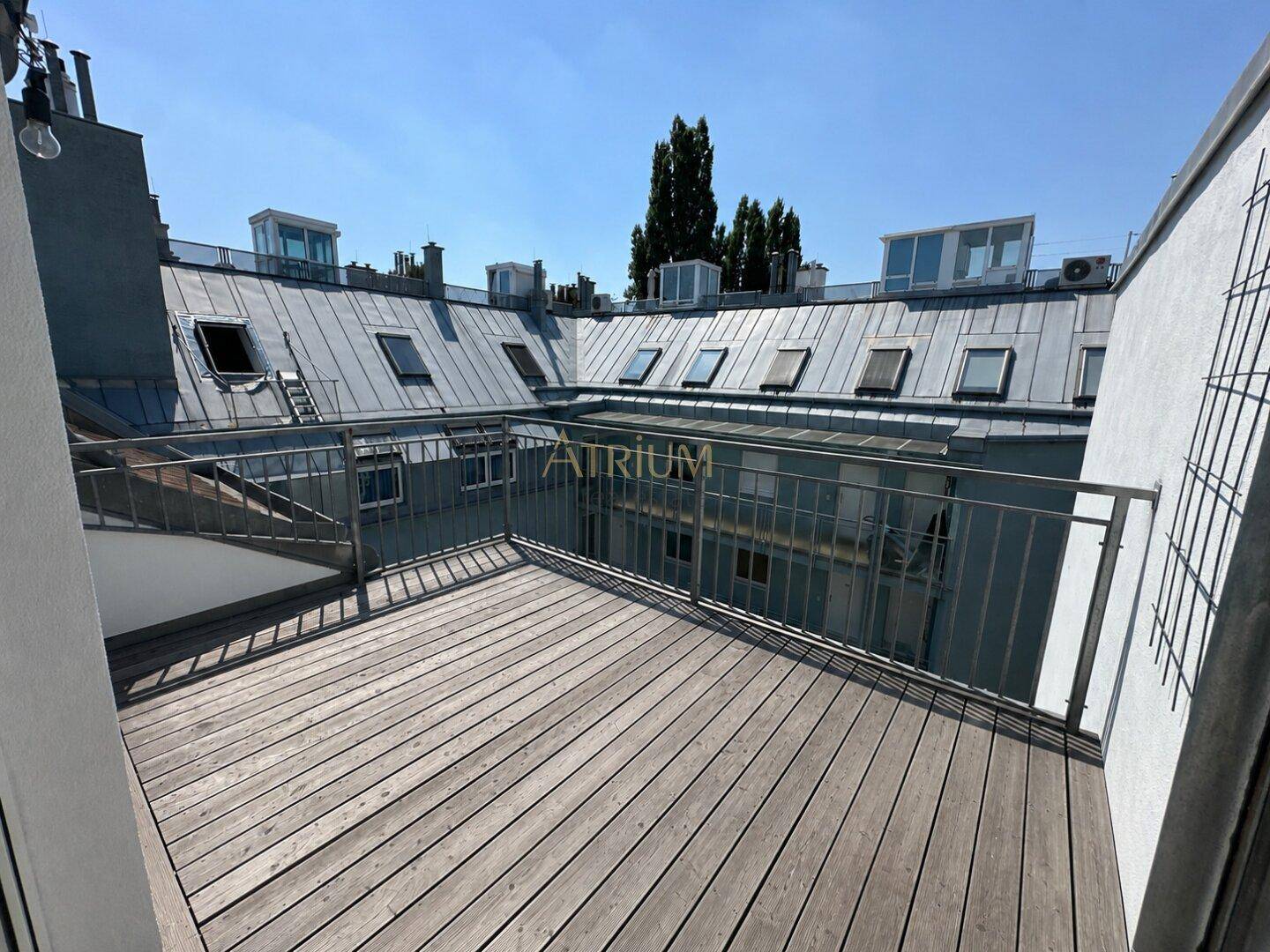 Unmöblierte Dachterrasse mit Holzboden und Blick auf die umliegenden Dächer und Gebäude.