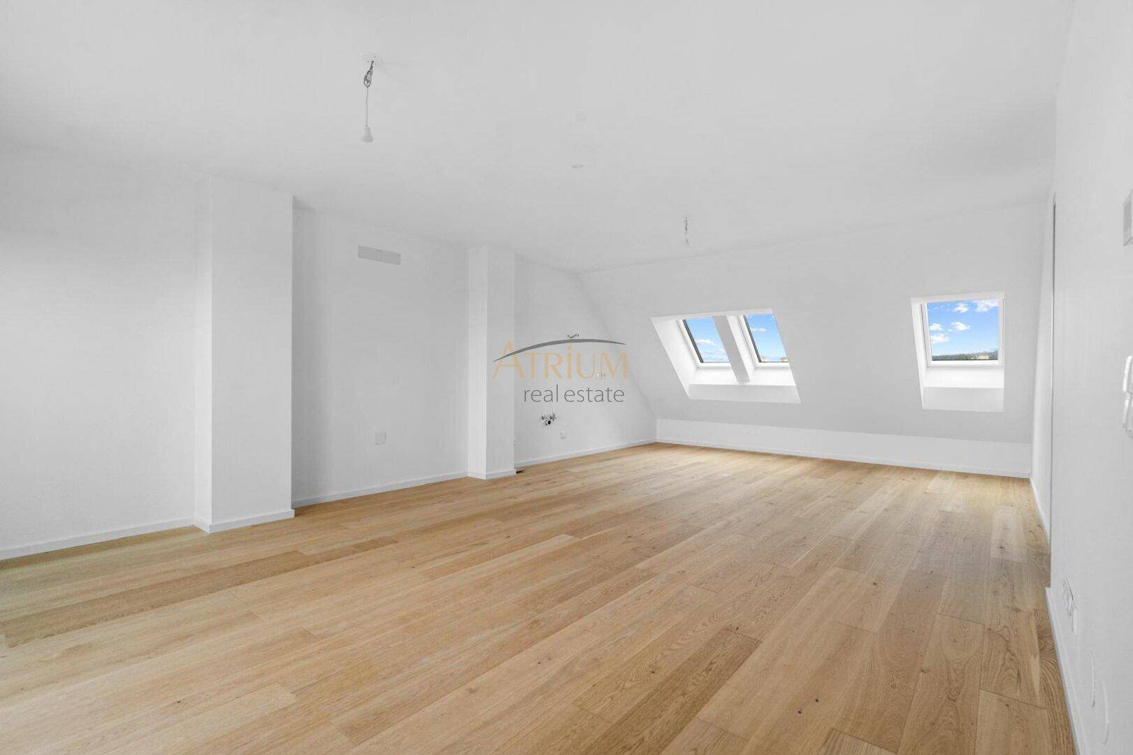 Geräumiger Raum im Dachgeschoss mit Holzboden, weißen Wänden und zwei Dachfenstern.