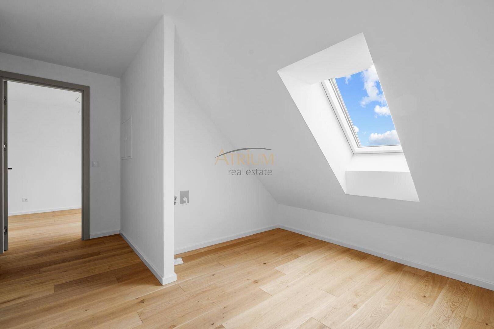 Heller Raum mit Dachschräge, Holzboden und einem großen Dachfenster.