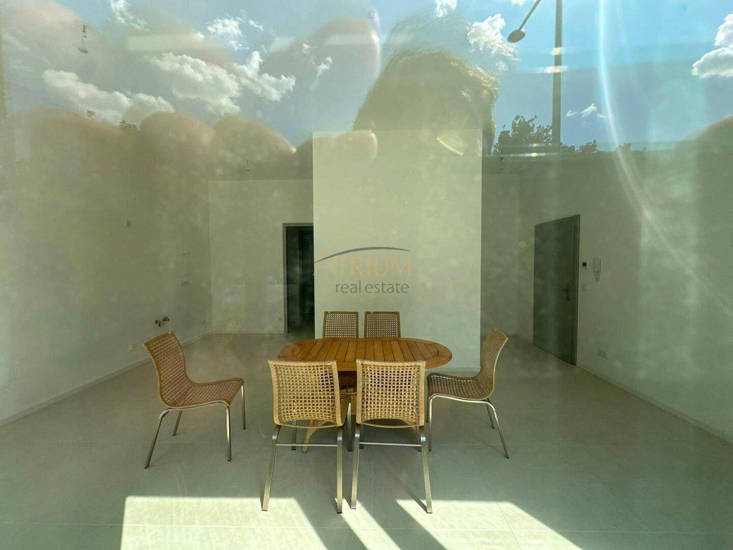 Heller Innenraum mit Tisch und Stühlen, durch die Fenster spiegelt sich der Himmel.