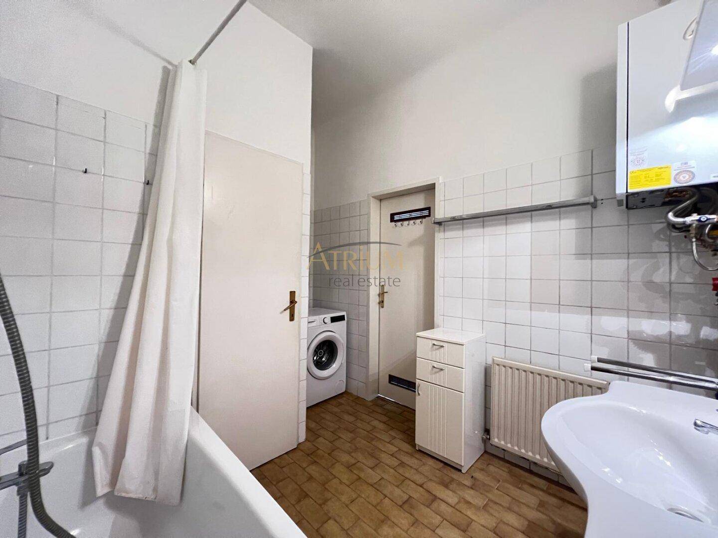 Funktionales Badezimmer mit Badewanne, Waschbecken und Waschmaschine, ausgestattet mit hellen Fliesen.