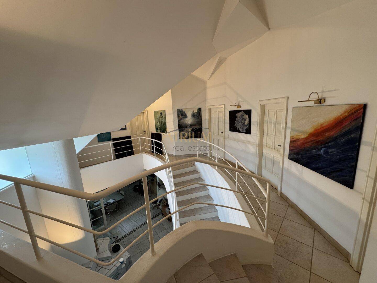 Elegantes Treppenhaus mit geschwungenem Geländer und Kunstwerken an den Wänden, verbindet die Etagen.