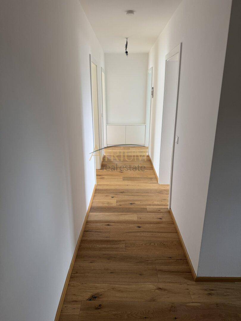 Heller Flur mit neuem Holzboden und weißen Wänden, der zu weiteren Räumen in der Wohnung führt.