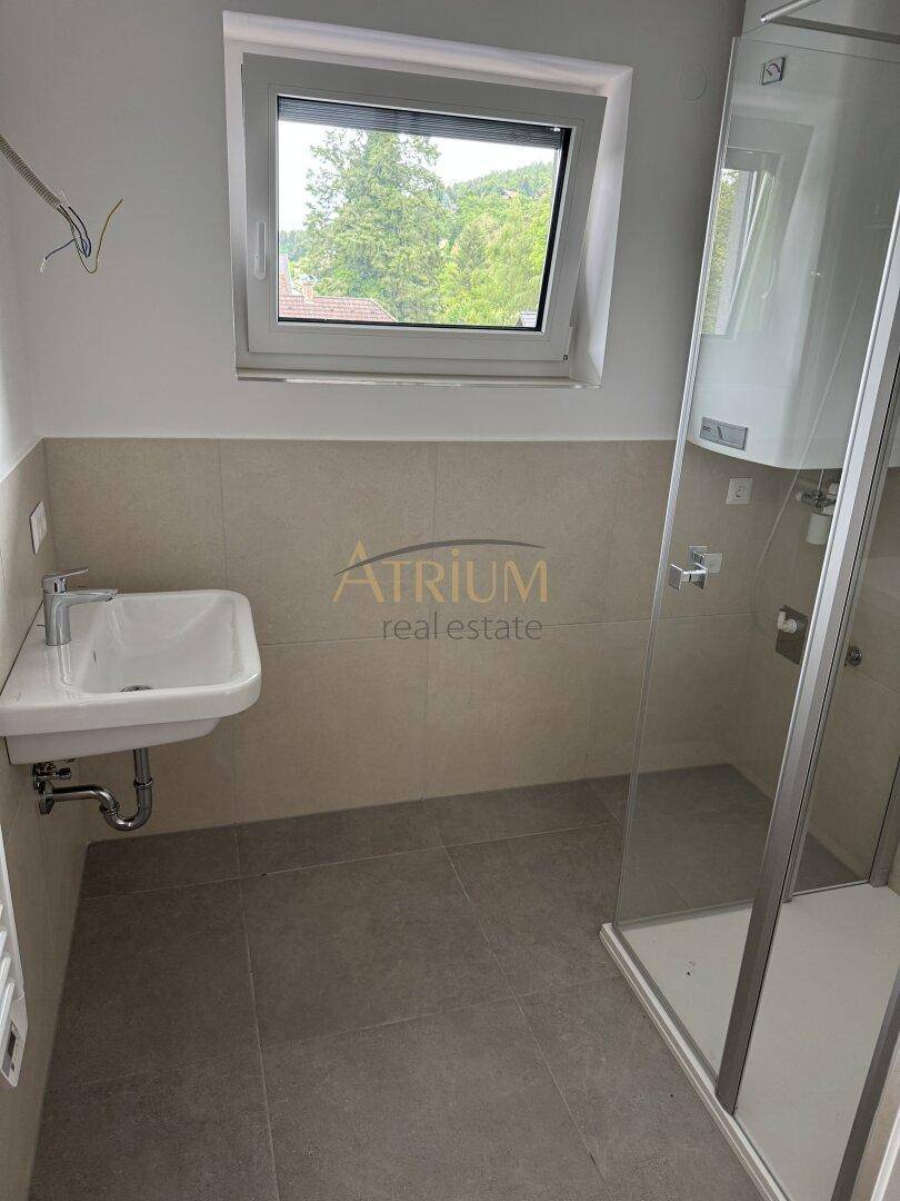 Modernes Badezimmer mit Duschkabine, Waschbecken und Fenster, hell gefliest in Beige und Grau.