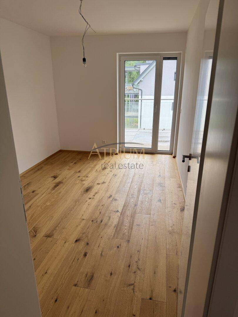 Leerer Raum mit Holzboden und einer großen Glastür, die Zugang zu einem Außenbereich bietet.