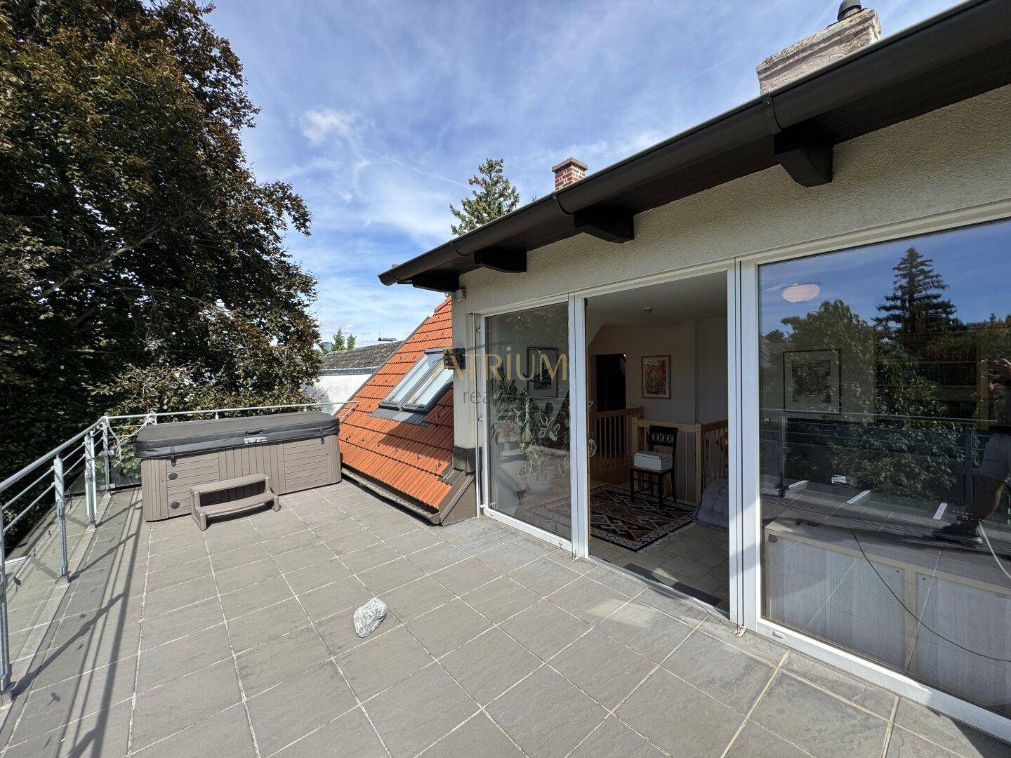Große Dachterrasse mit Fliesenboden und einem Whirlpool, zugänglich durch Glasschiebetüren.