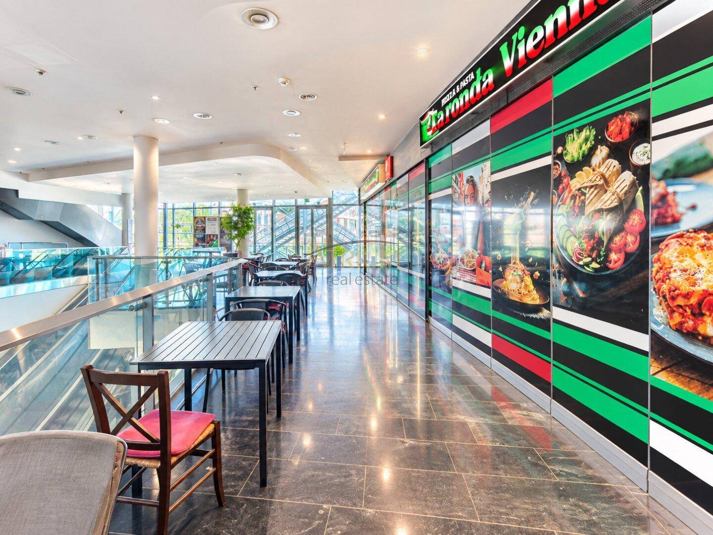 Heller, offener Gastronomiebereich in einem Einkaufszentrum mit Tischen und einem Imbissstand.