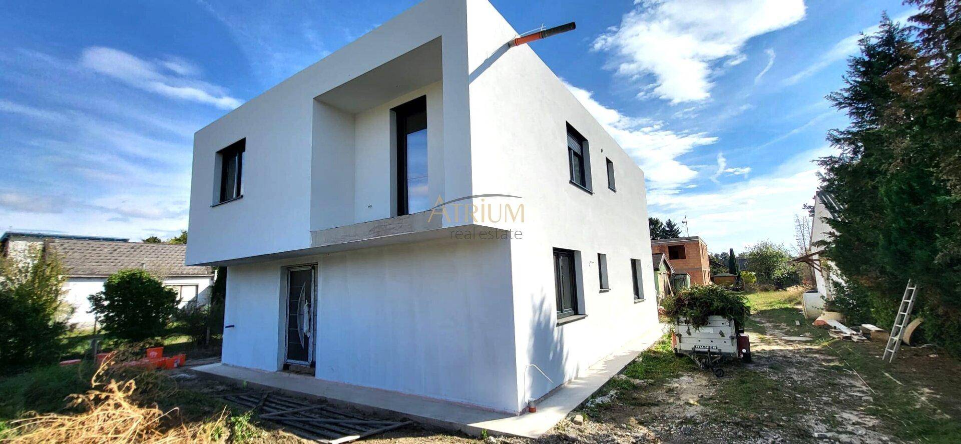 Ansicht der modernen weißen Hausfassade mit dunklen Fensterrahmen und minimalistischem Design unter blauem Himmel.