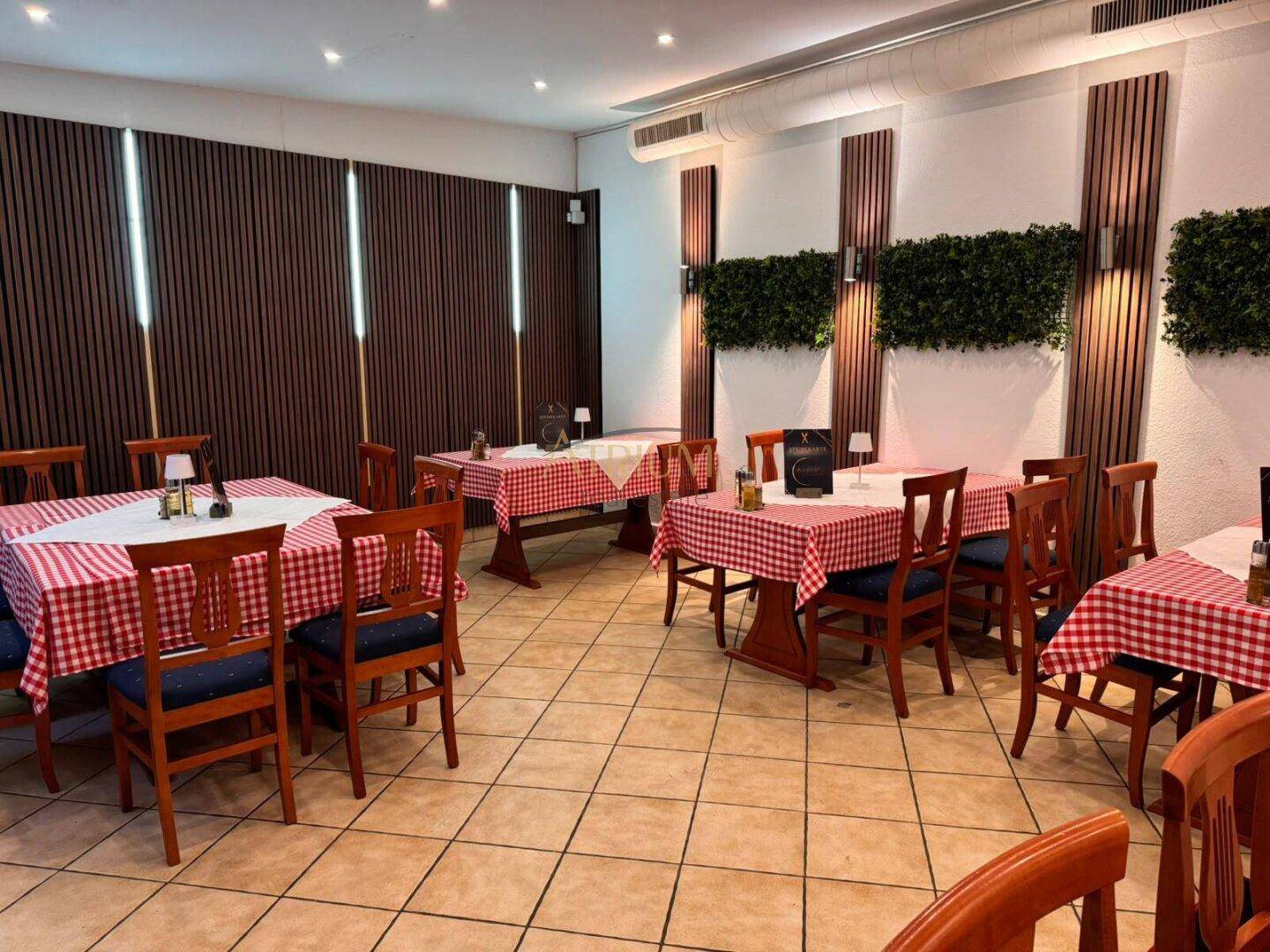 Heller Restaurant-Speisesaal mit mehreren Tischen, Fliesenboden, Holzstühlen und dekorativen Wandelementen.