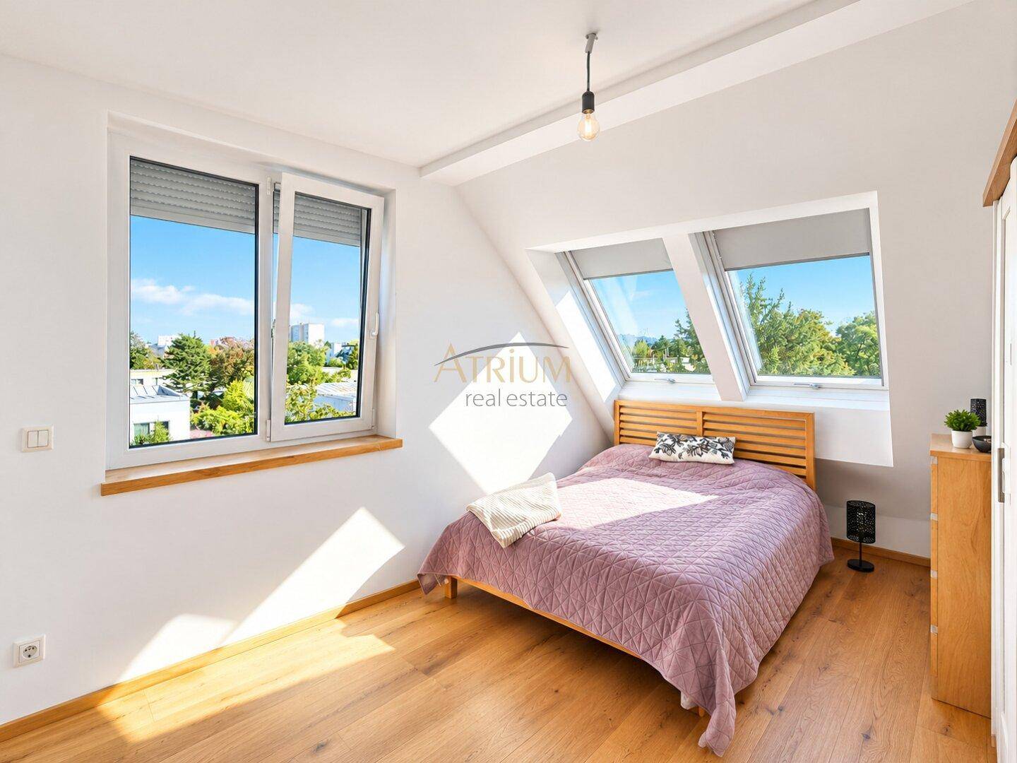 Helles Schlafzimmer mit Holzboden, Dachschrägen und mehreren Fenstern, inklusive Dachfenstern.
