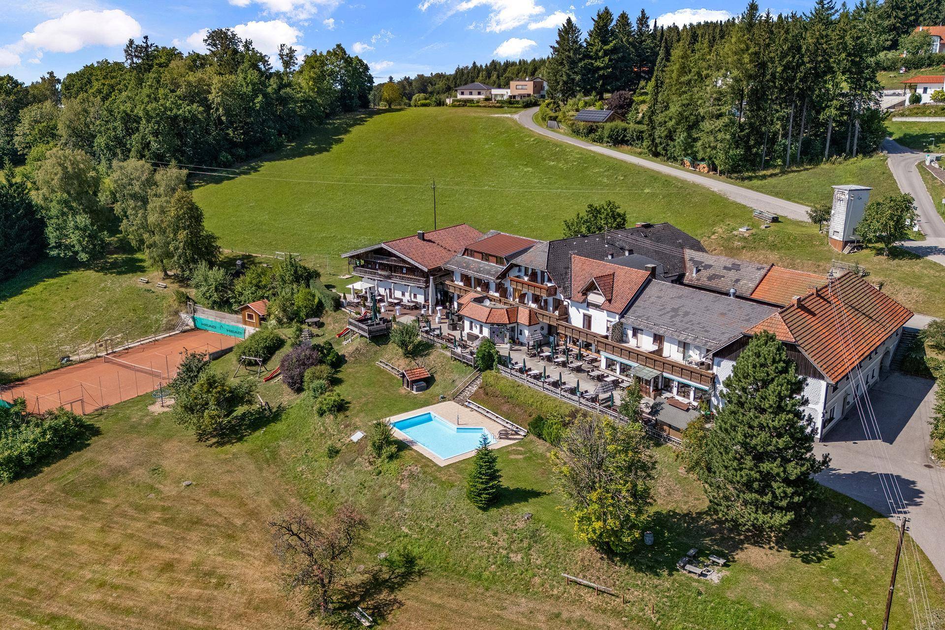 Weitläufige Luftaufnahme des Anwesens mit Hauptgebäude, Tennisplatz und Pool in ländlicher Umgebung.