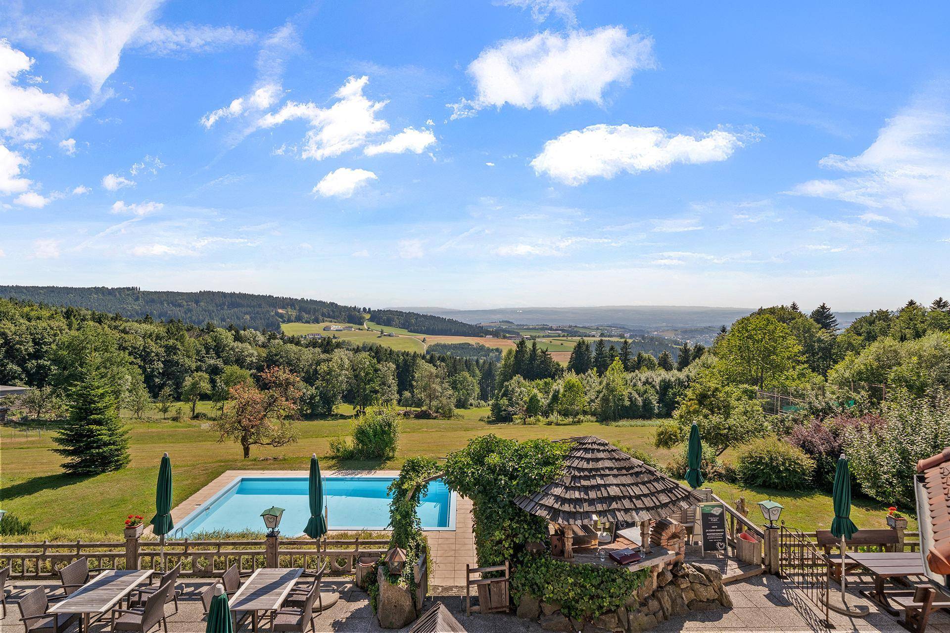 Terrasse mit Poolblick und einem überdachten Sitzbereich, umgeben von grüner Natur.