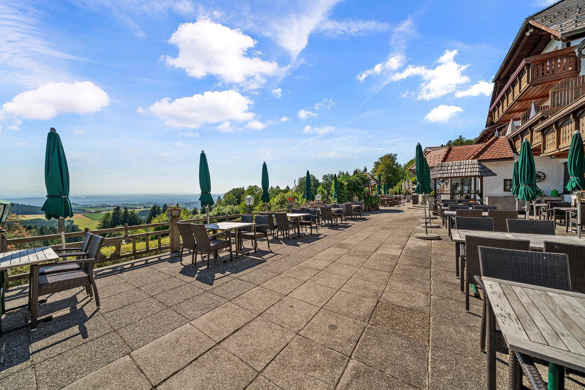 Lange Außenterrasse mit Tischen, Stühlen und Sonnenschirmen, die einen Panoramablick bietet.