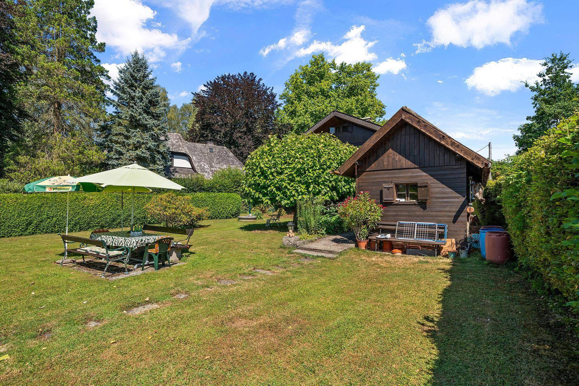 Sonnige Gartenanlage mit Rasen, Sitzgruppe und einem rustikalen Holzschuppen neben dem Haupthaus.