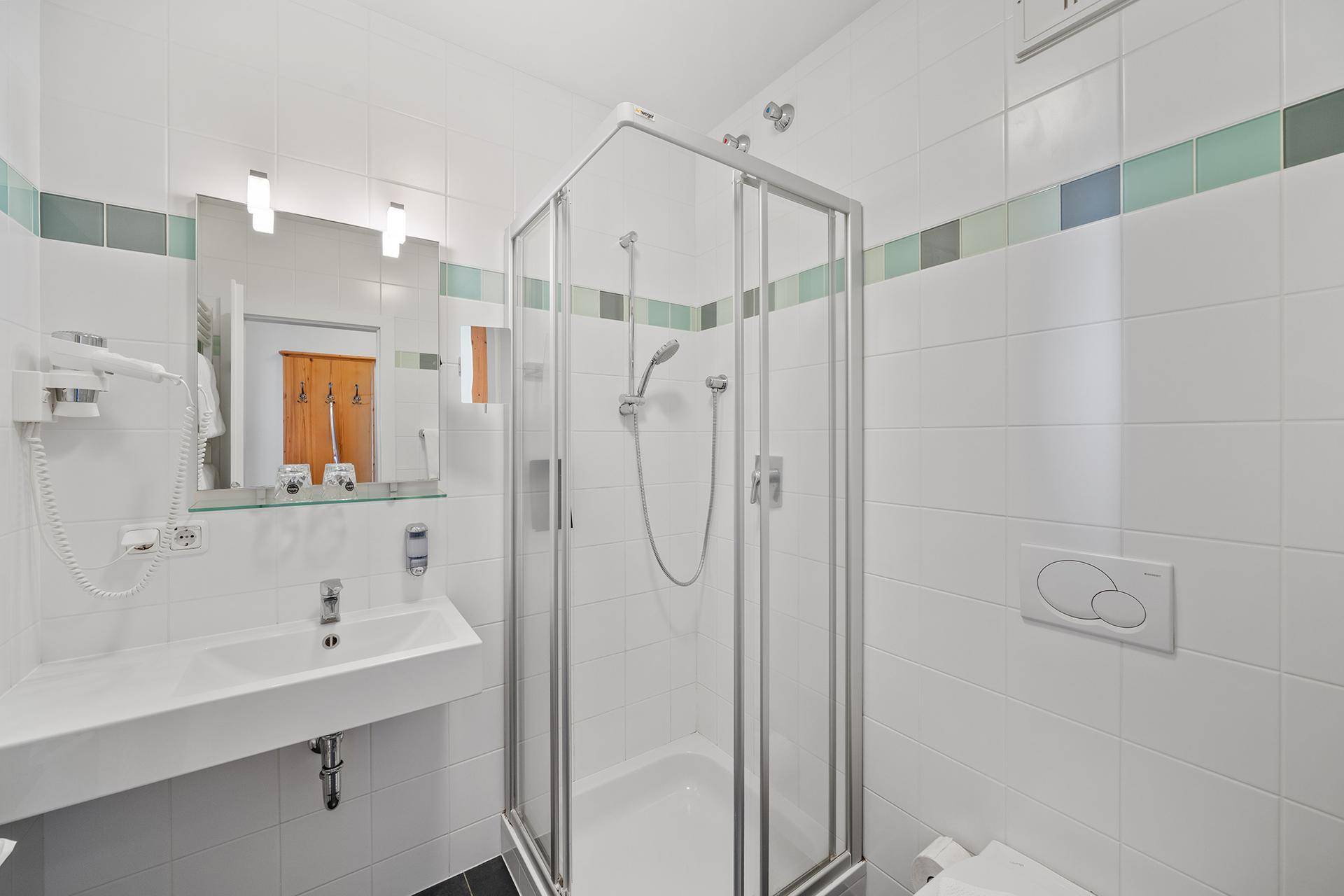 Helles Badezimmer mit moderner Duschkabine, Waschbecken und Wand-WC, ausgestattet mit weißen Fliesen.