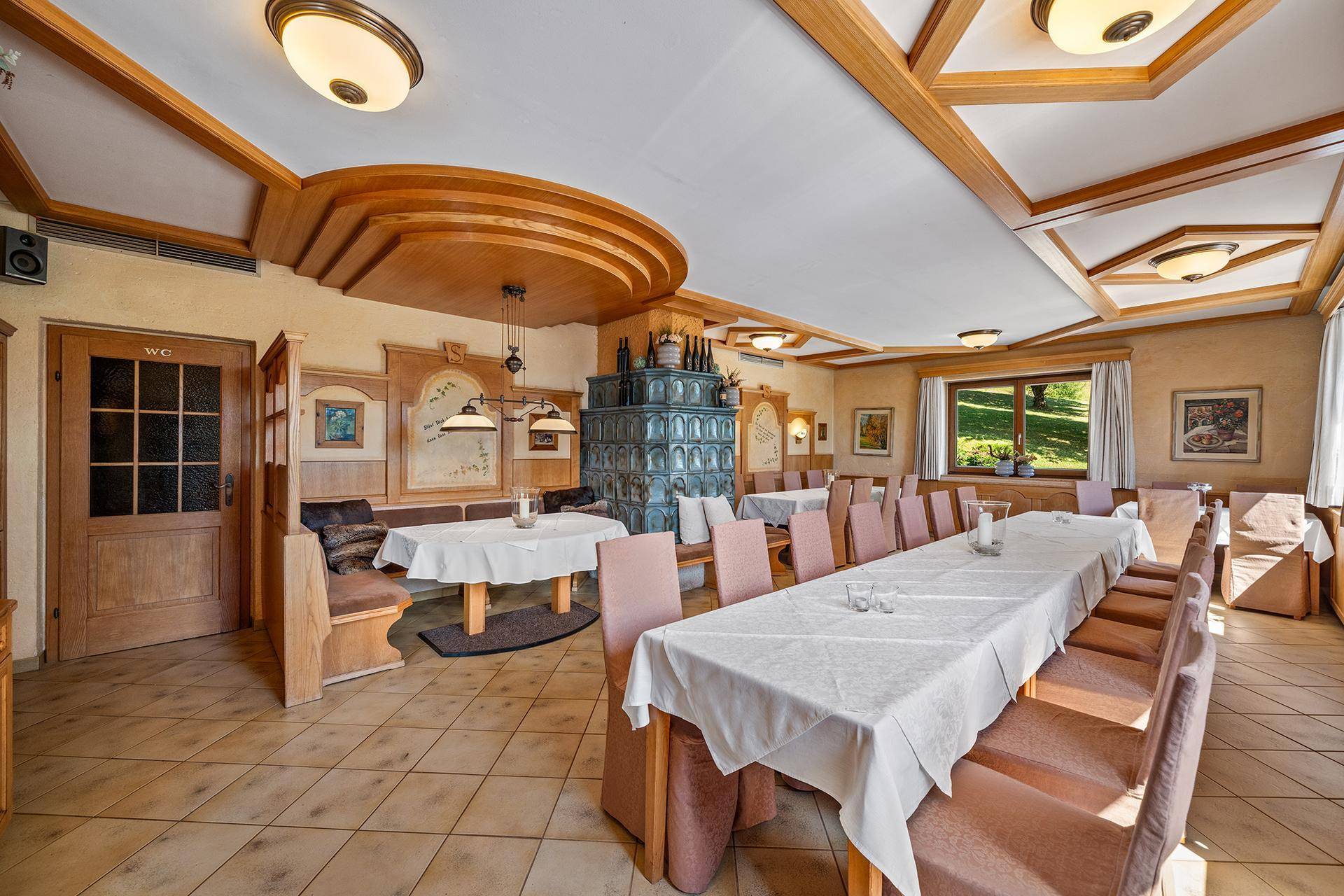 Eleganter Speisesaal mit traditionellem Kachelofen, Holzelementen und festlich gedeckten Tischen.