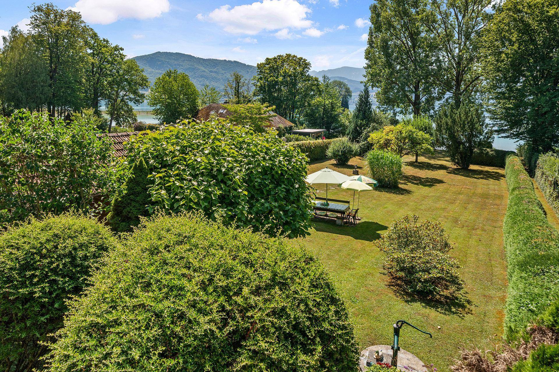 Gepflegter Gartenbereich mit Rasen, Sträuchern und einer gemütlichen Sitzgruppe unter Sonnenschirmen.